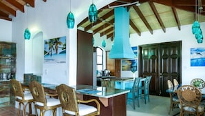 Una cocina con una isla central, taburetes de bar y lámparas colgantes color turquesa.
