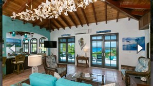Un salón espacioso con techo alto, un ventanal con vistas al mar, un televisor y una zona de estar acogedora con un sofá turquesa.