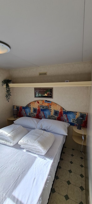 A neatly made bed with white linens and pillows, a colorful headboard, a bedside lamp, and a small plant on the nightstand.