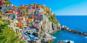 A coastal town with colorful buildings, a rocky shoreline, and a clear blue sea.