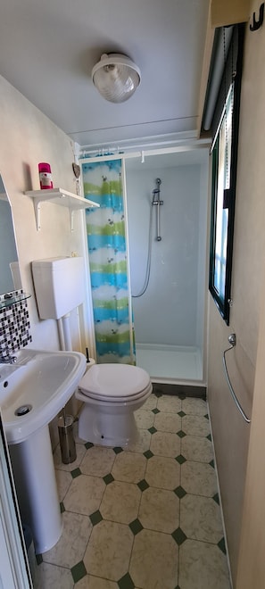 A small bathroom with a toilet, sink, shower, and a window.