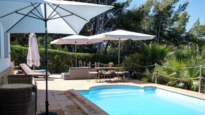A pool area with lounge chairs, umbrellas, and a dining set.