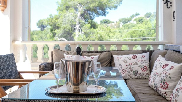 A room with a glass table, a metal punch bowl, and a sofa with floral cushions.