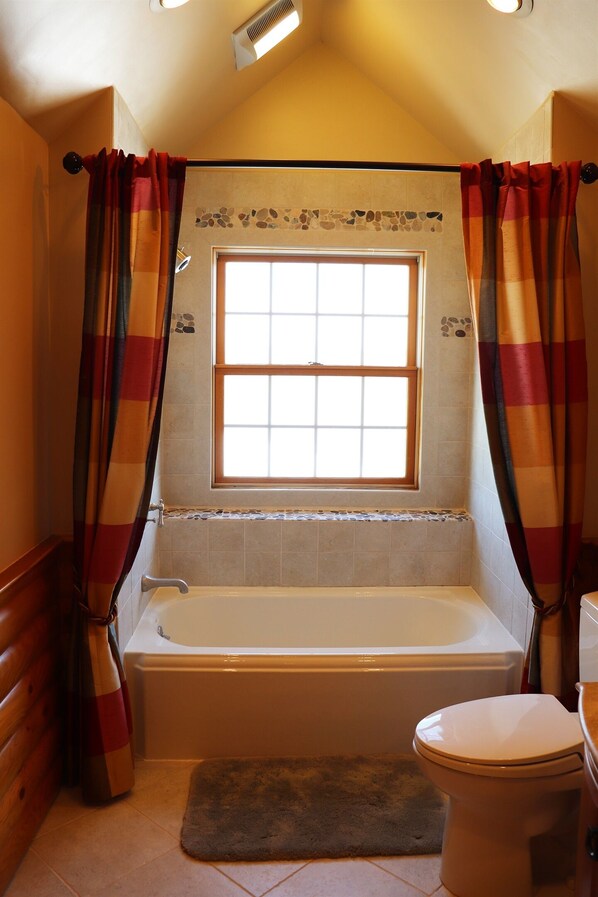 Un baño con bañera, inodoro y ventana con cortinas.