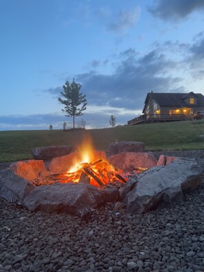 A fire pit with rocks and a house in the background. - Skyview Acres - Stunning 360° views, a short drive to Cooperstown (Burlington Flats)