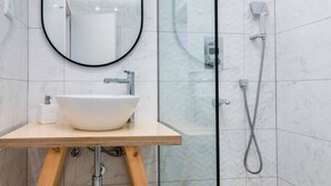 Un baño moderno con tocador de madera, un espejo redondo y ducha con cerramiento de vidrio.