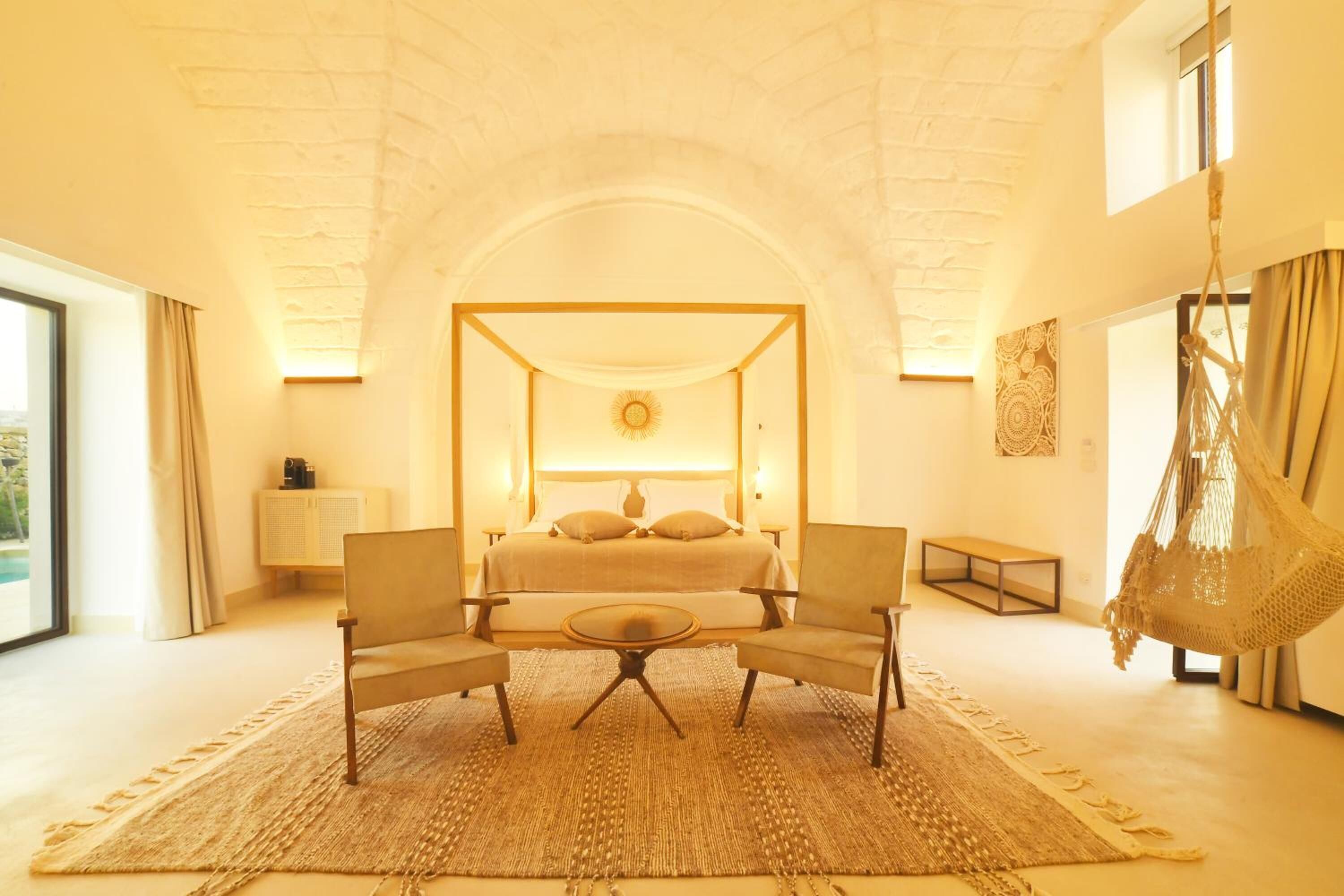 A bedroom with a four-poster bed, a sitting area with two chairs and a table, and a hanging chair.