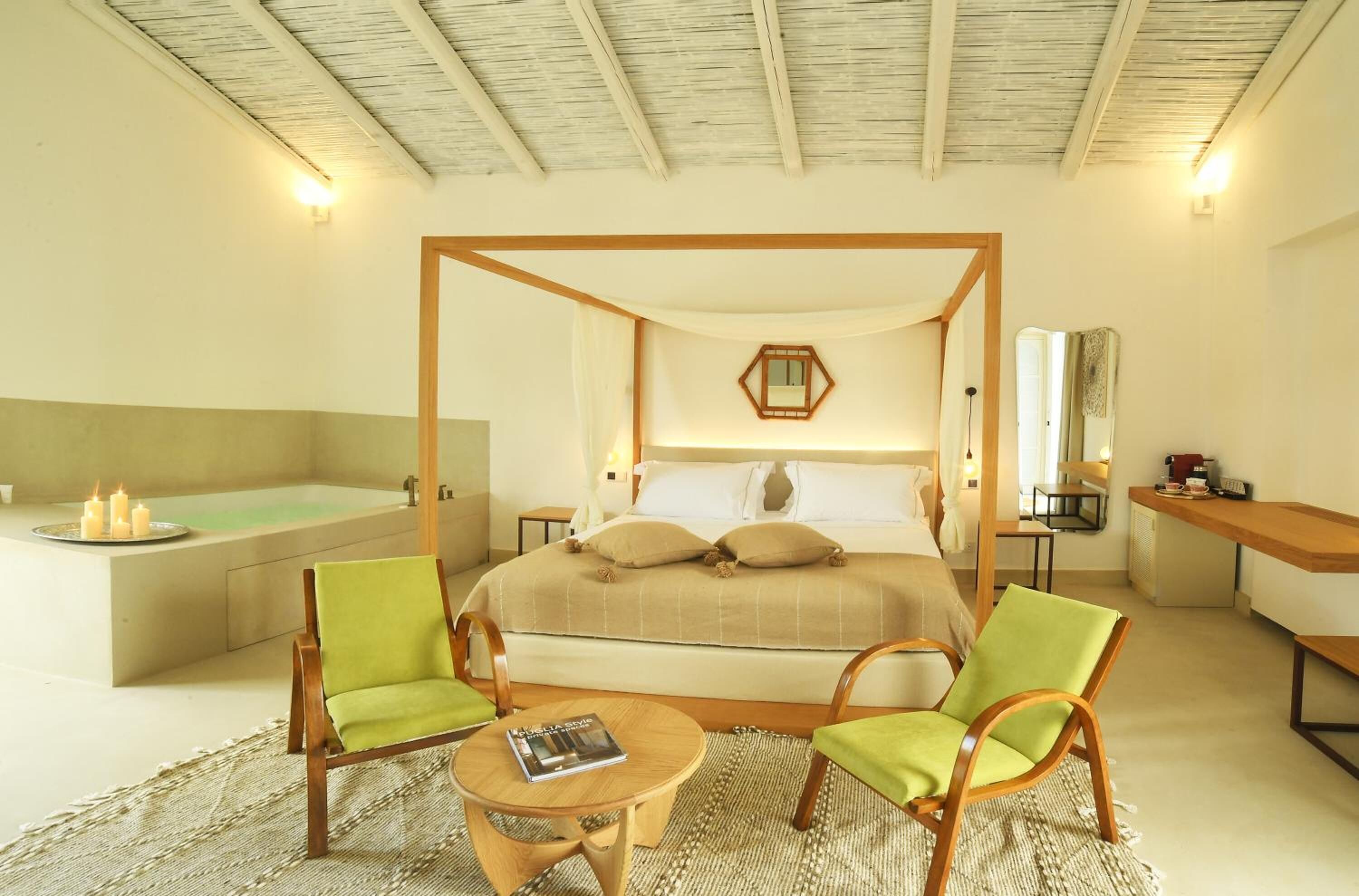 Une chambre à coucher avec un lit à baldaquin, un coin salon avec deux fauteuils, une petite table ronde et une baignoire.