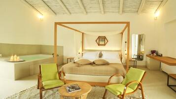 Une chambre à coucher avec un lit à baldaquin, un coin salon avec deux fauteuils, une petite table ronde et une baignoire.