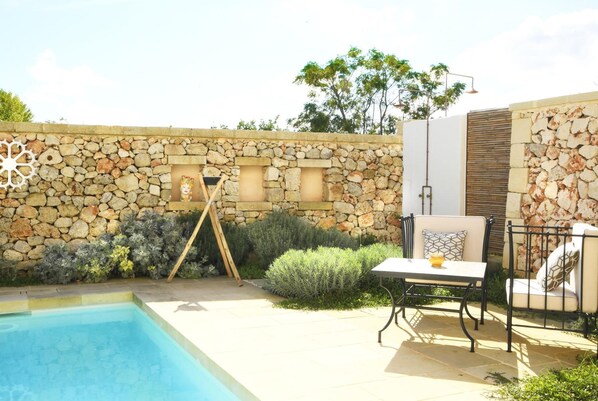 A poolside area with a stone wall, a swing set, and outdoor furniture.