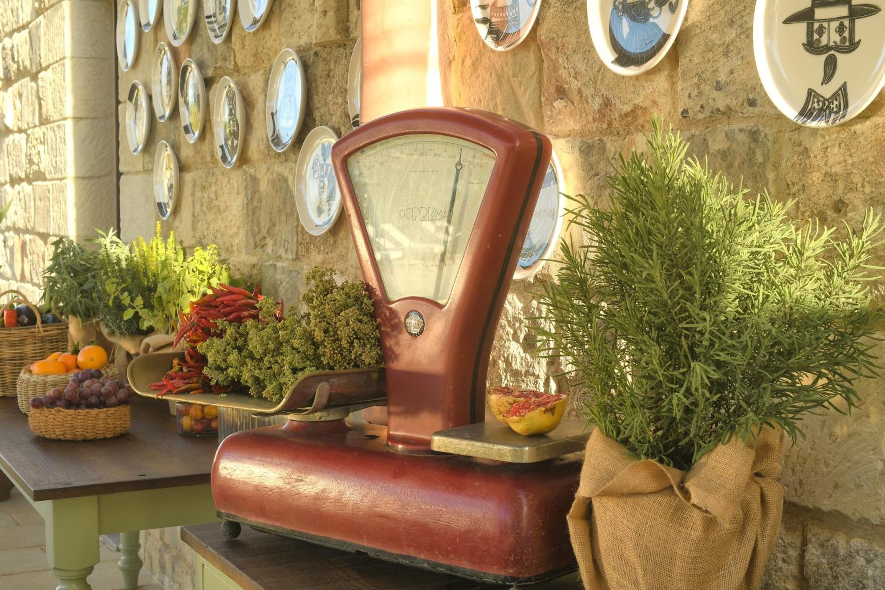 A vintage scale with fresh produce and decorative plates on a stone wall.