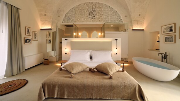 A spacious bedroom with a large bed, a bathtub, and a high arched ceiling.