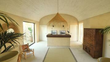Un hall d’entrée spacieux avec un plafond haut, un comptoir de réception, un meuble en bois et une grande plante en pot.