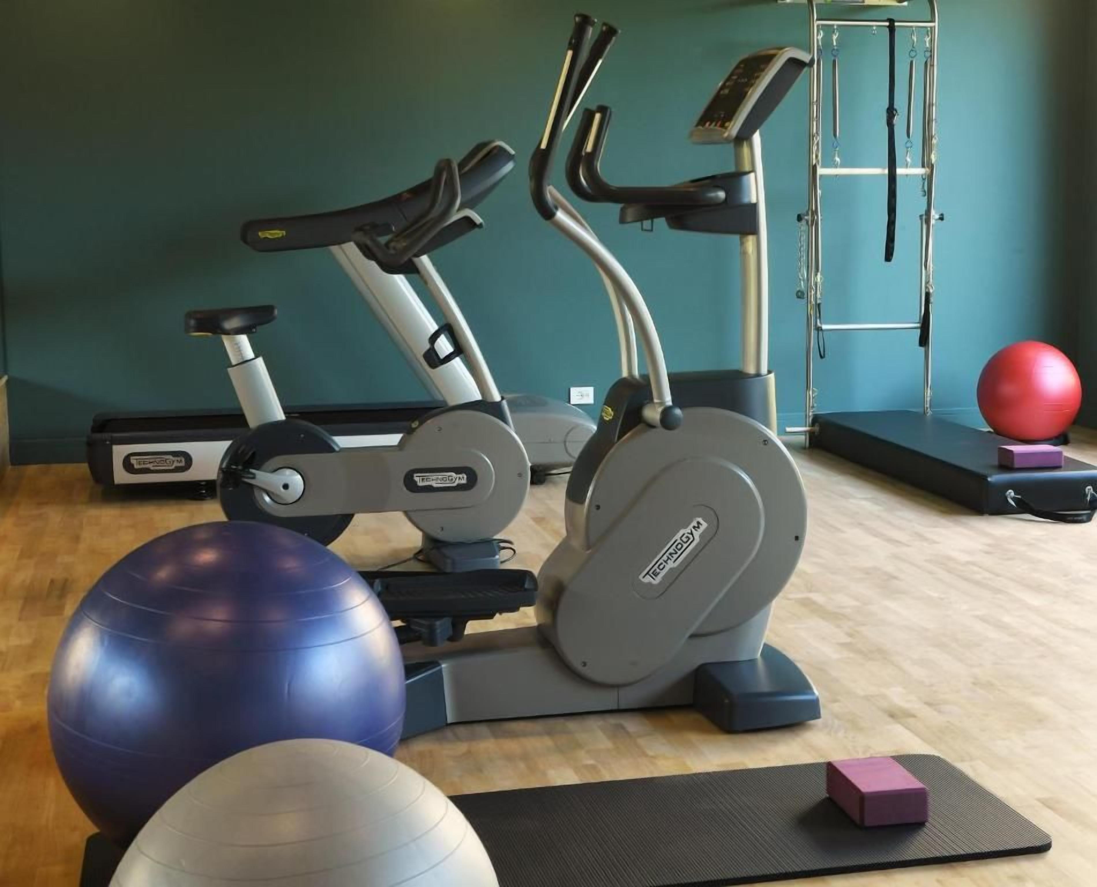 Un gimnasio con equipo de ejercicio, incluyendo cintas de correr, bicicletas estáticas y pelotas de ejercicio.