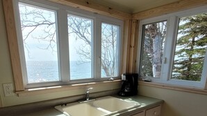 Una cocina con pileta doble, muebles de madera y ventanas amplias con vistas a los árboles y al cielo.