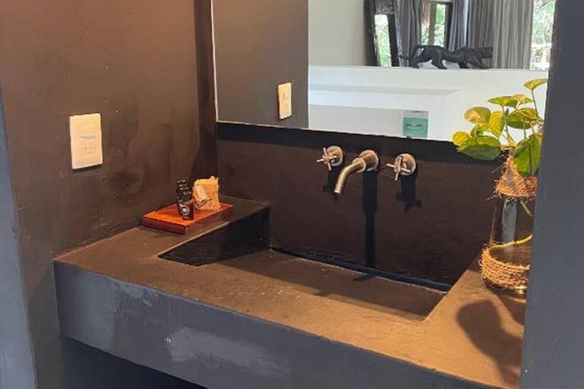 Un baño con un lavamanos oscuro, un espejo y un cubo de basura.