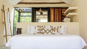 Une chambre avec un grand lit, une échelle en bois, un luminaire suspendu et une vue sur la verdure.