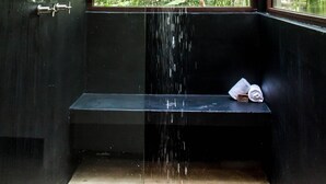 Une salle de bain moderne dotée d’une douche à pluie, d’un banc et d’une fenêtre donnant sur un espace verdoyant.