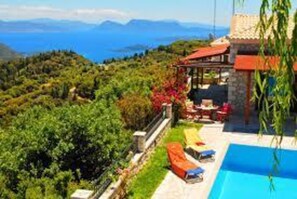 Área da piscina com vista para montanhas, espaço coberto para sentar e um edifício de pedra.