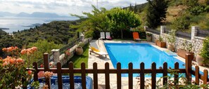 A swimming pool with a wooden fence, surrounded by potted plants and a view of a mountainous landscape. - Executive Villa Scorpios With Private Pool (Lefkada)