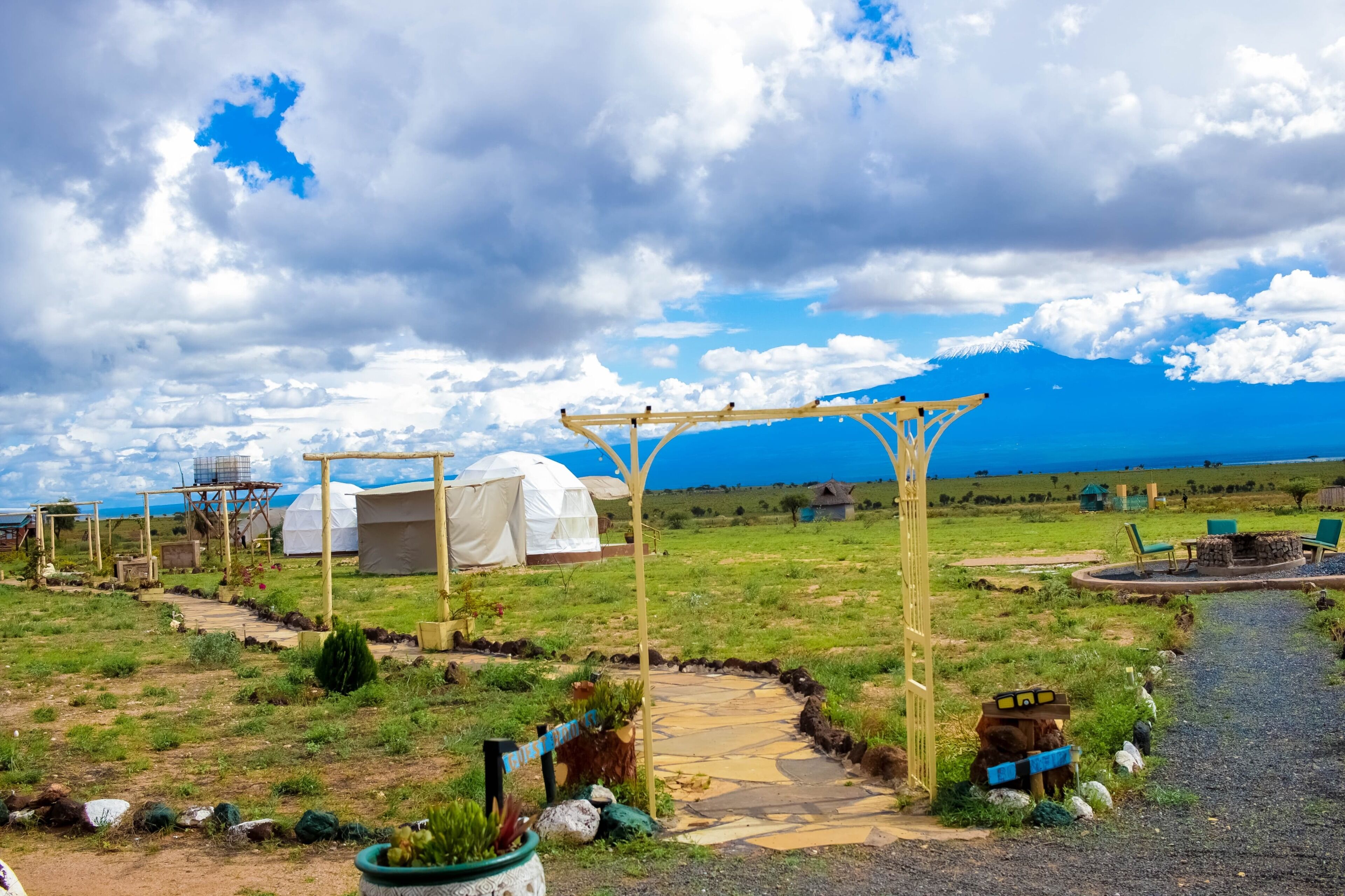 A rural outdoor setting with yurts, a wooden pergola, and a gravel path.