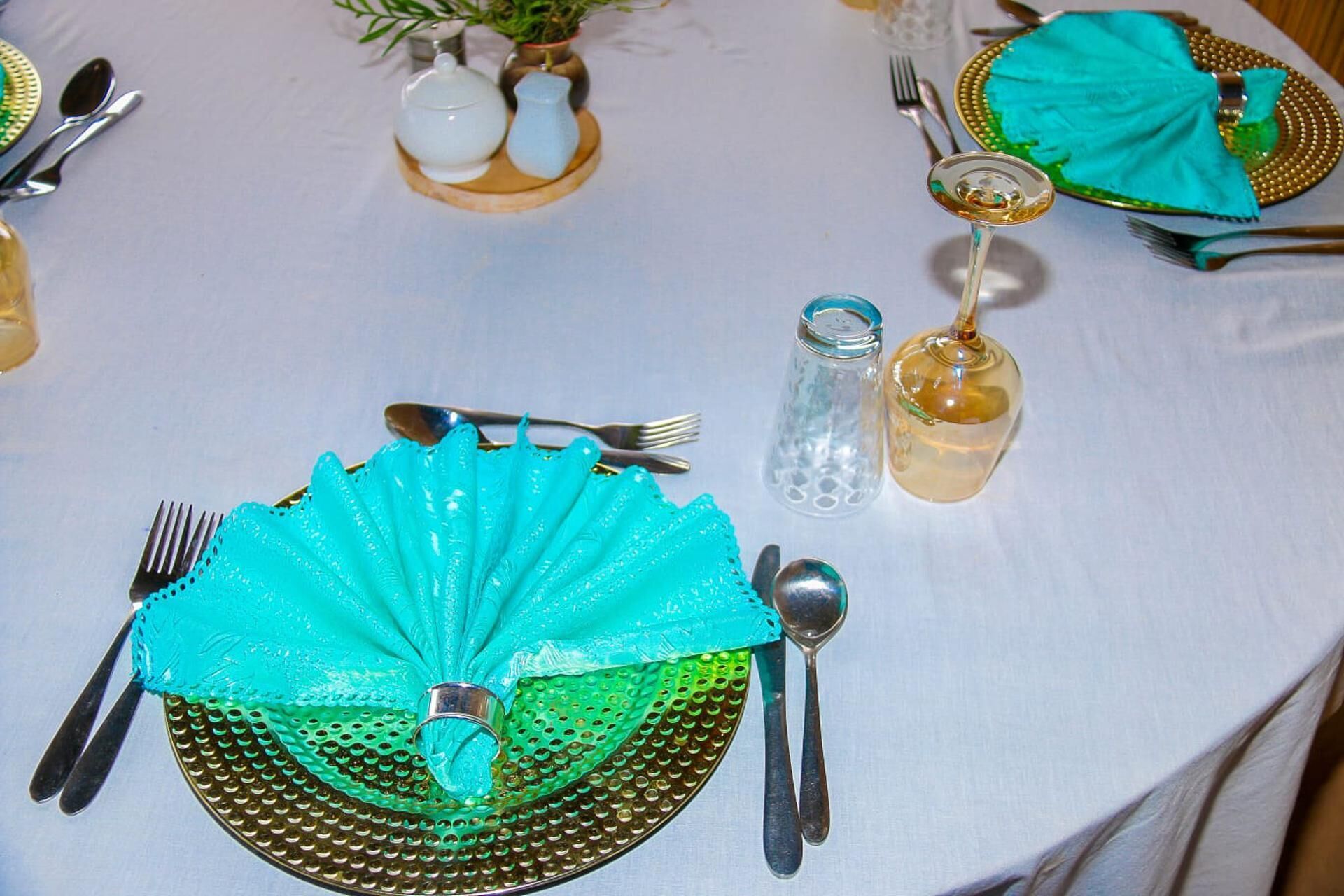A table set with turquoise napkins, a green glass plate, and silverware.