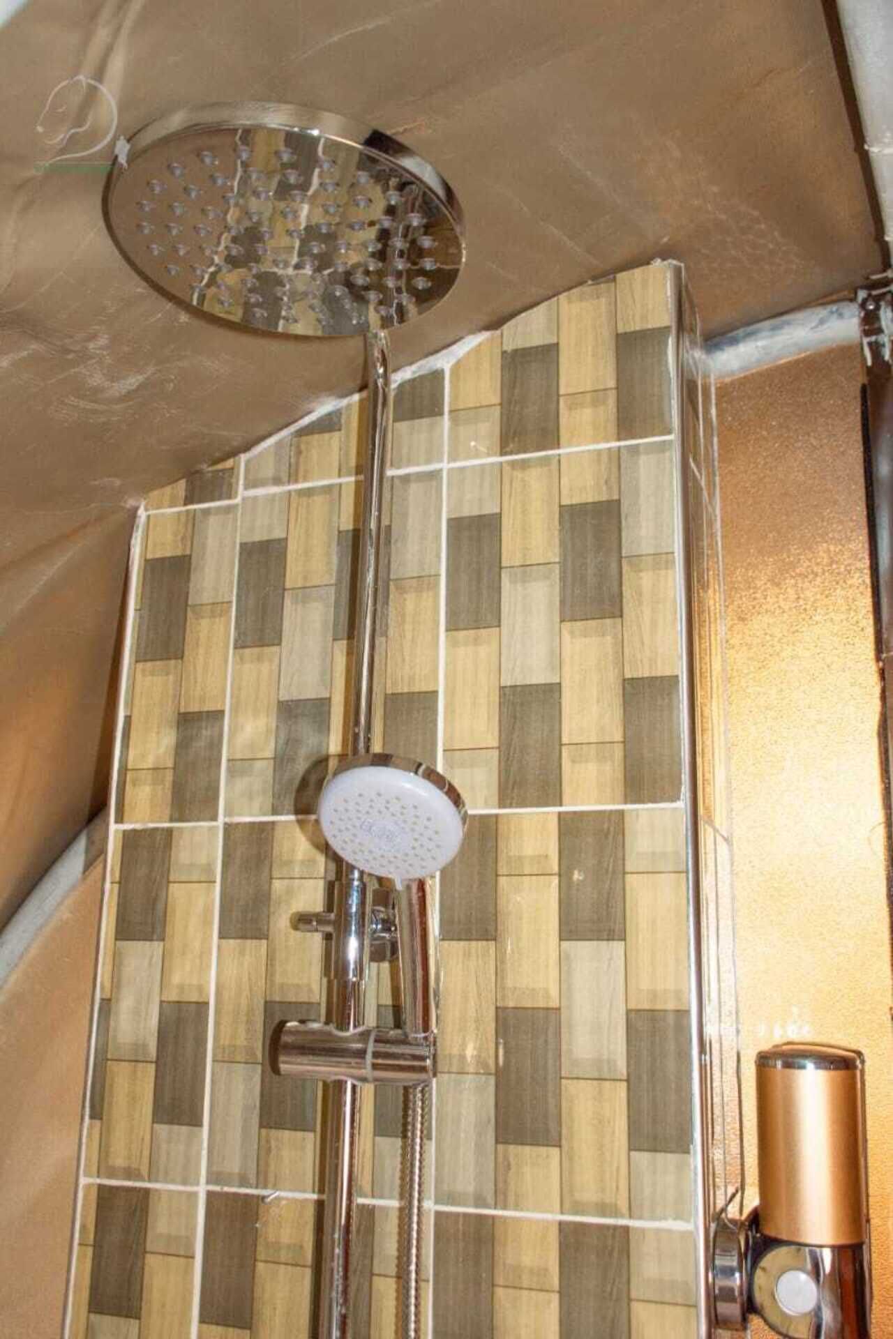 A shower with a rain head and a handheld showerhead, mounted on a tiled wall with a checkered pattern.
