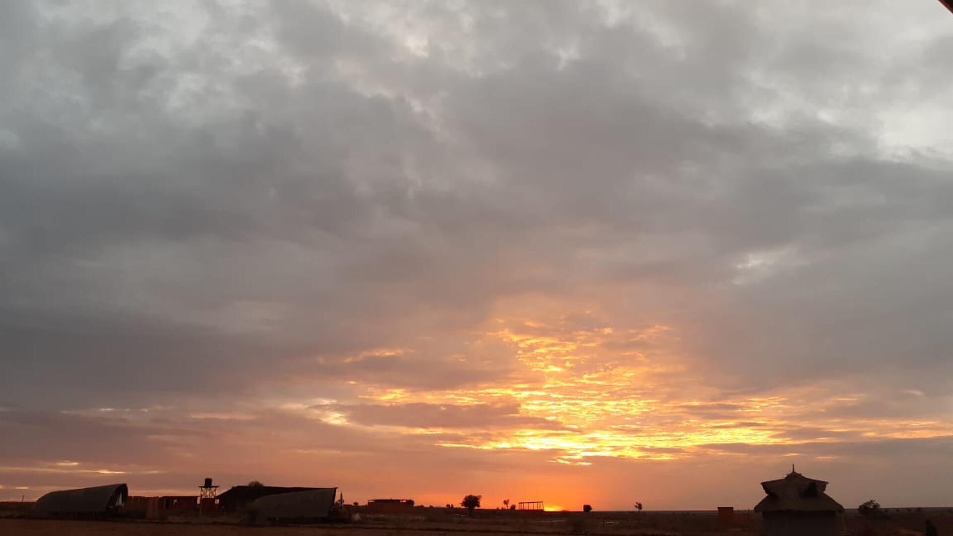 Solnedgang over et landligt landskab med bygninger og åbne marker.