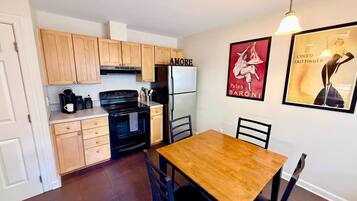 A compact kitchen with wooden cabinets, a black stove, and a white refrigerator. There is a wooden dining table with chairs.
