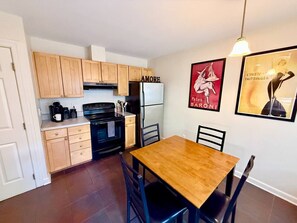 A compact kitchen with wooden cabinets, a black stove, and a white refrigerator. There is a wooden dining table with chairs. - Chic Condo in Downtown Raleigh (Raleigh)