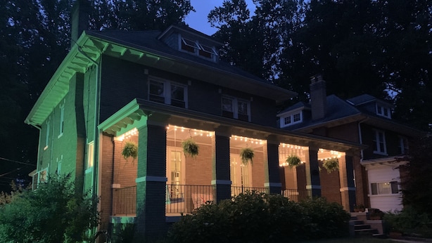 Una casa de dos pisos con un porche, luces colgantes y plantas suspendidas.