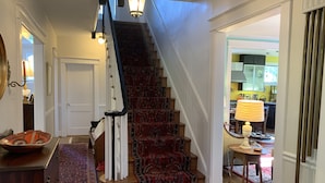 Una escalera con alfombra estampada que sube a un segundo piso, un banco de madera con un cuenco decorativo y una alfombra en el suelo.