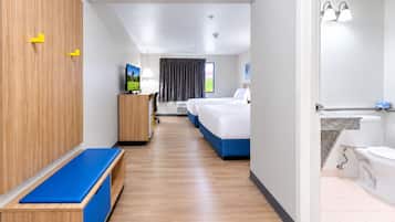 A hotel room with a wooden wardrobe, a desk with a television, a bed with a blue headboard, and a bathroom with a bathtub and toilet.