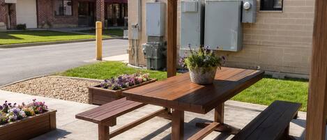 Un patio al aire libre con una mesa y bancos de madera, rodeado de macetas con flores.