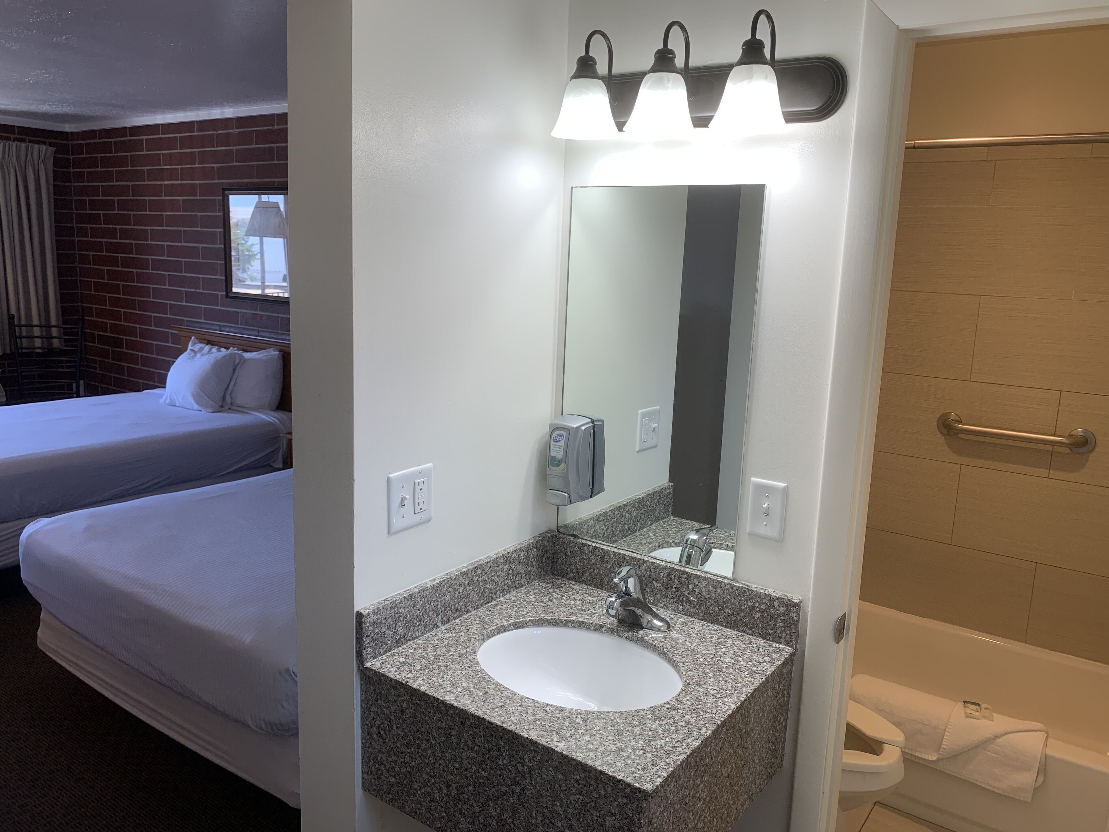 A hotel room with a bed, a bathroom with a sink, mirror, and a shower.