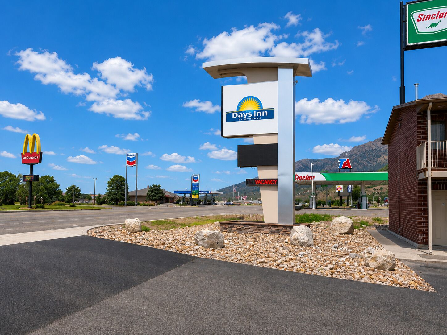 A Days Inn sign, a McDonald's sign, a Chevron sign, and a Sinclair sign at a gas station.