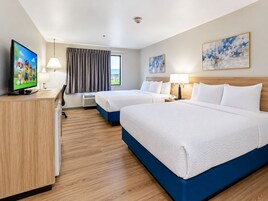 Una habitación de hotel con dos camas, un escritorio, un televisor y una ventana con cortinas.