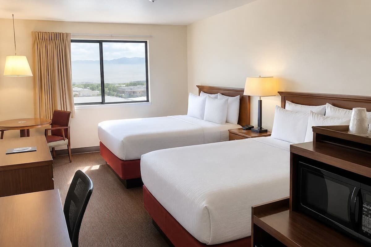 A hotel room with two beds, a desk, a chair, a TV, and a window with a view.