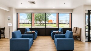 A room with blue sofas, round tables, and large windows with a view of trucks and a tree. - Days Inn by Wyndham Lake Point (Tooele)