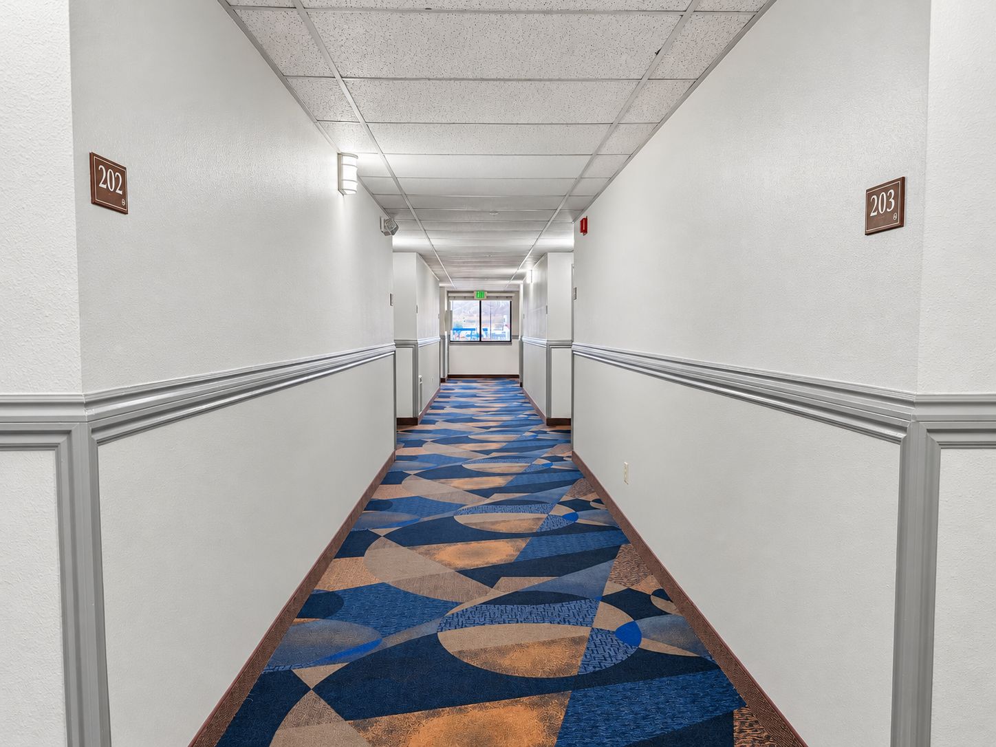 A hotel hallway with a patterned carpet, white walls, and numbered doors.