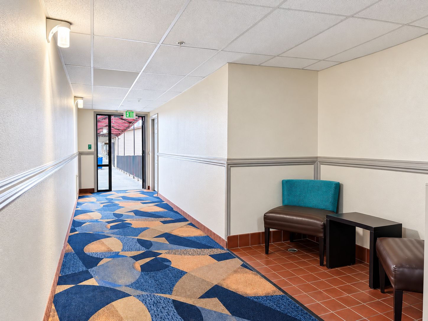 A hotel corridor with patterned carpet, a bench, and a table.