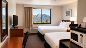 A hotel room with two beds, a desk, a television, a microwave, and a large window with a mountain view. - Days Inn by Wyndham Lake Point (Tooele)