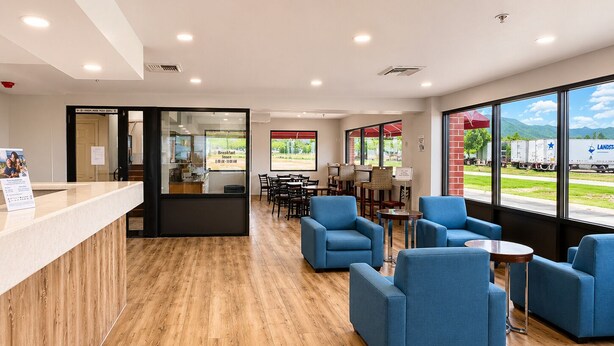 A modern reception area with a wooden floor, blue seating, and large windows offering a view of the outside. - Days Inn by Wyndham Lake Point (Tooele)