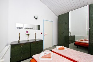 Une chambre d’hôtel moderne, équipée d’un lit, d’une table de chevet agrémentée d’un vase de fleurs, d’une commode et d’un grand miroir.