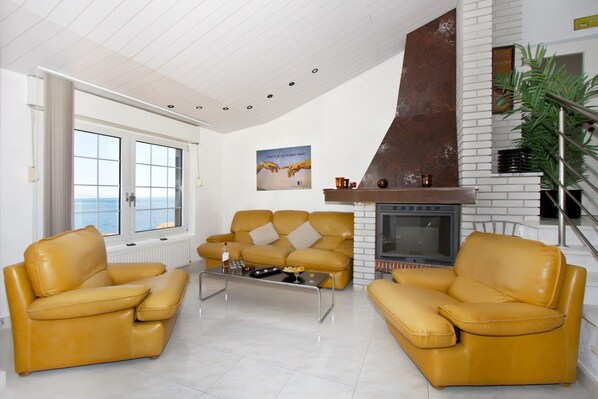Un salon avec deux canapés en cuir jaune, une table basse, une cheminée et une vue sur la mer grâce à de grandes fenêtres.
