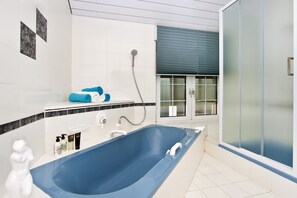 Une salle de bain moderne avec une baignoire bleue, une douche et une douche à l’italienne avec des parois en verre.