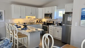 A modern kitchen with white cabinets, a central island with seating, stainless steel appliances, and a view of the outdoors. - 3 Bed/2.5 Bath 1450 sq ft with Large Open Floor Plan, 3 Min Walk to Beach (Emerald Isle)
