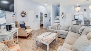 A spacious living room with a large sofa, a coffee table, and a television. There is a kitchen area with a dining table and chairs.