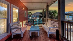 A covered porch with wooden benches and a table, overlooking a scenic view of houses and palm trees.