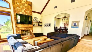 A spacious living room with a stone fireplace, a large sectional sofa, and a dining area with a wooden table and chairs. - Waterfront Luxury Home on 5 Acres. 
Sleeps 22. Beds: 5 king, 4 queen, 4 twin XL (New Braunfels)